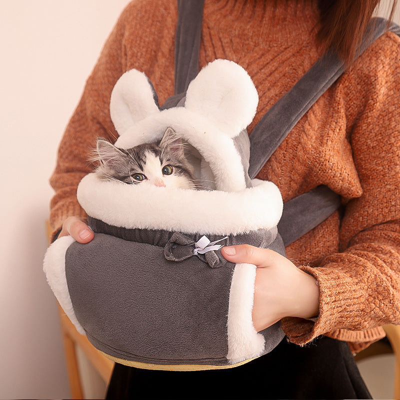 Cat in a bunny-style carrier held by a person wearing an orange sweater.