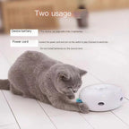 Cat playing with a white feather toy on a tiled floor, with text about device battery and power cord usage.