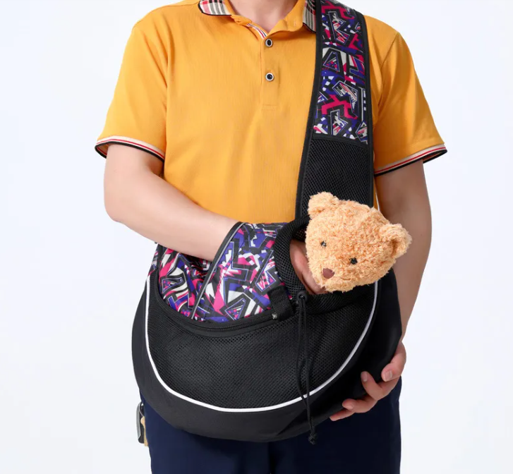 Person holding a black pet carrier with a colorful patterned strap, containing a teddy bear.