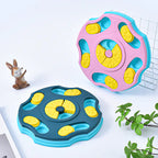 Two colorful dog and cat puzzle toys with yellow centers on a white surface, accompanied by a small figurine and plant.
